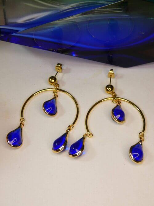 Boucles d'oreilles en arc de cercle doré et gouttes bleues. Bijou Sophia Célesta