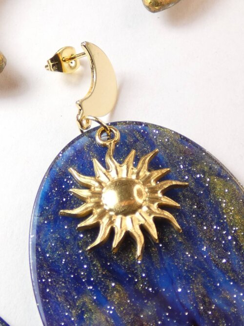 Boucles d'oreilles lune et soleil sur pendentif ovale bleu nuit à paillettes. Bijou Sophia Célesta