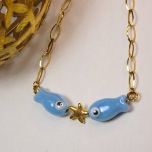 Bracelet original aux anneaux plats dorés avec deux poissons en céramique bleu entourant une étoile de mer dorée. Bijou en exemplaire unique Sophia Célesta