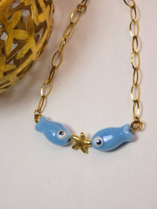 Bracelet original aux anneaux plats dorés avec deux poissons en céramique bleu entourant une étoile de mer dorée. Bijou en exemplaire unique Sophia Célesta