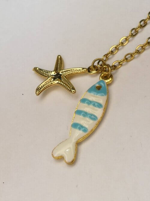 Collier en acier inoxydable doré avec pendentif poisson en résine bleue et blanche et étoile de mer dorée. Collier réversible. Bijou en exemplaire unique Sophia Célesta