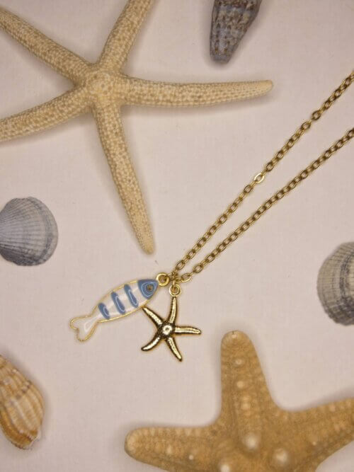 Collier en acier inoxydable doré avec pendentif poisson en résine bleue et blanche et étoile de mer dorée. Collier réversible. Bijou en exemplaire unique Sophia Célesta