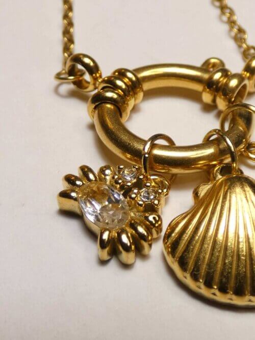 Collier doré avec attache bouée devant à laquelle sont suspendus une breloque crabe, une en forme de coquillage et la dernière en forme de tortue. Bijou en exemplaire unique Sophia Célesta